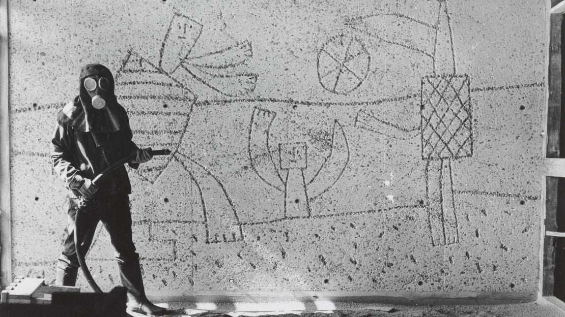 Carl Nesjar sandblåser Picassos motiver i Høyblokka, antagelig i 1959. Mann i drakt som sandblåser motiver i betongvegg