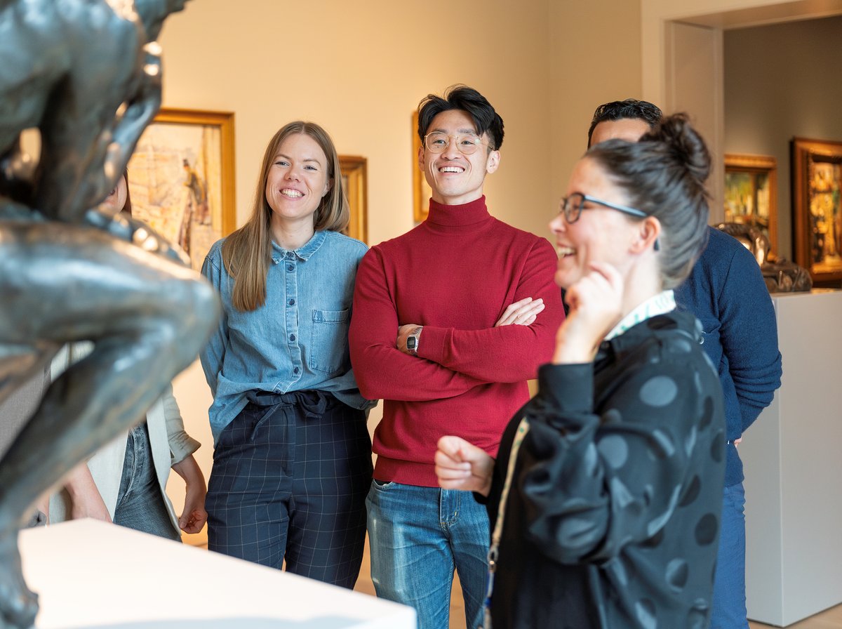 Bildet viser fire smilende mennesker som ser på en skulptur