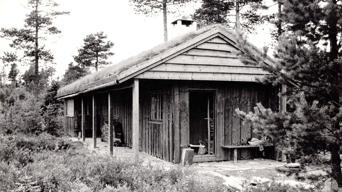 Wenche Selmer og Jens Selmer, Hytte på Ringkollen, 1953 Et sort-hvitt bilde av en trehytte, omgitt av skog