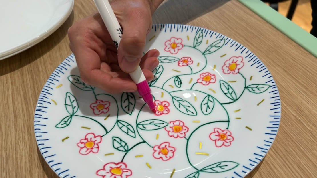 Hånd med tusj som tegner blomster på en hvit tallerken
