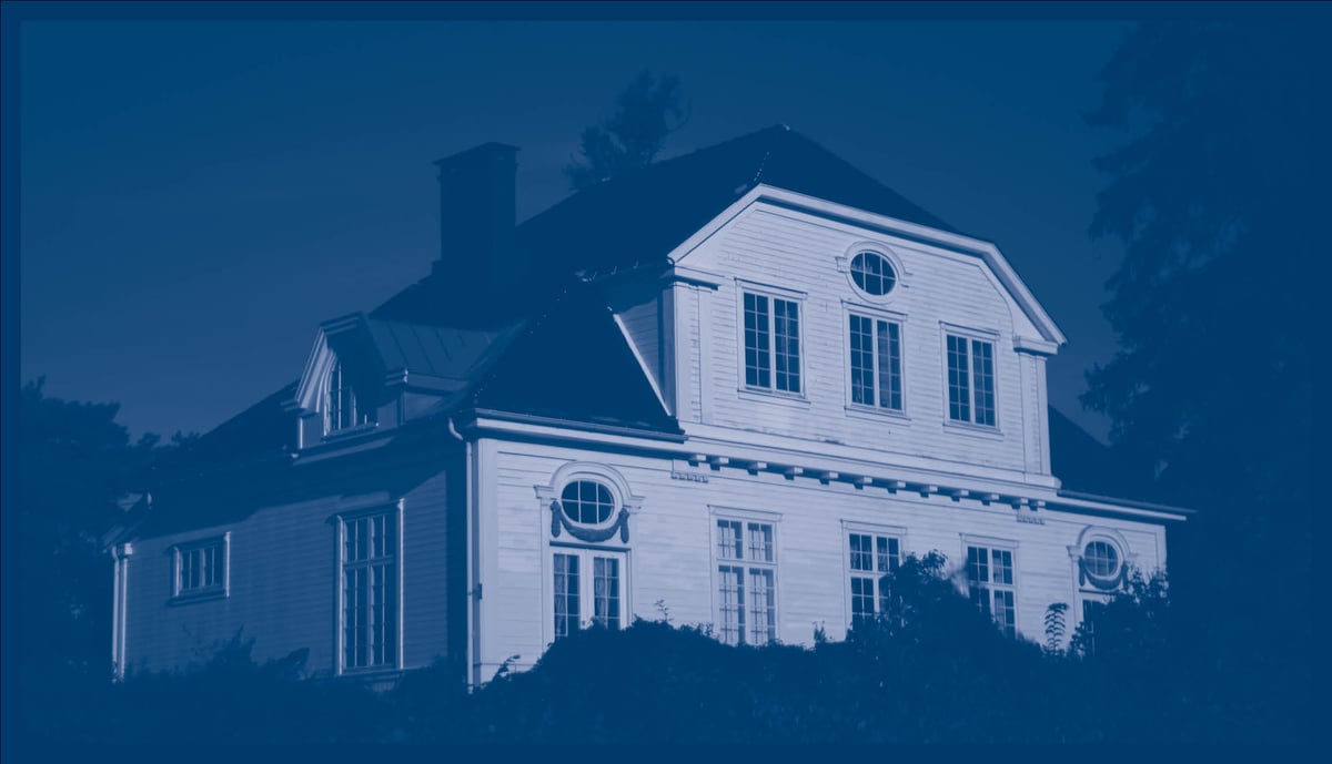 Bildet viser et stort hvitt trehus fra 1904, med skog omkring. 