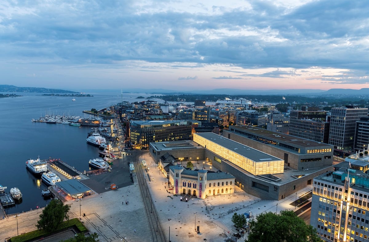 Stort museumsbygg ved fjorden med lysende avlang hall på toppen