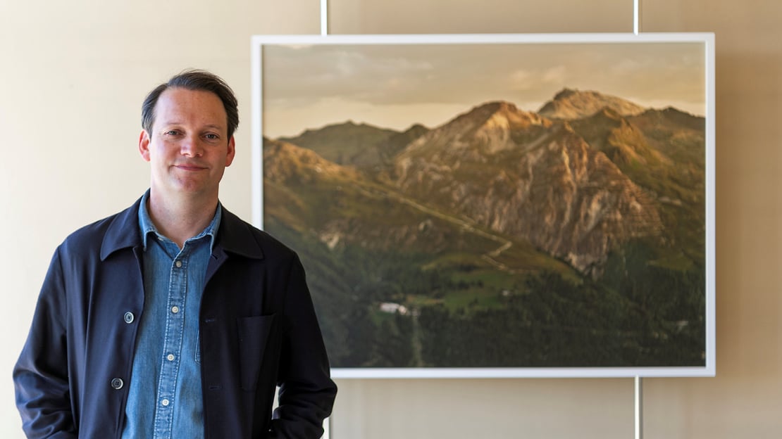 Espen Gleditsch Kunstner Espen Gleditsch står ved siden av et av sine fotografier av et fjellandskap der et tuberkulosesanatorium skimtes.