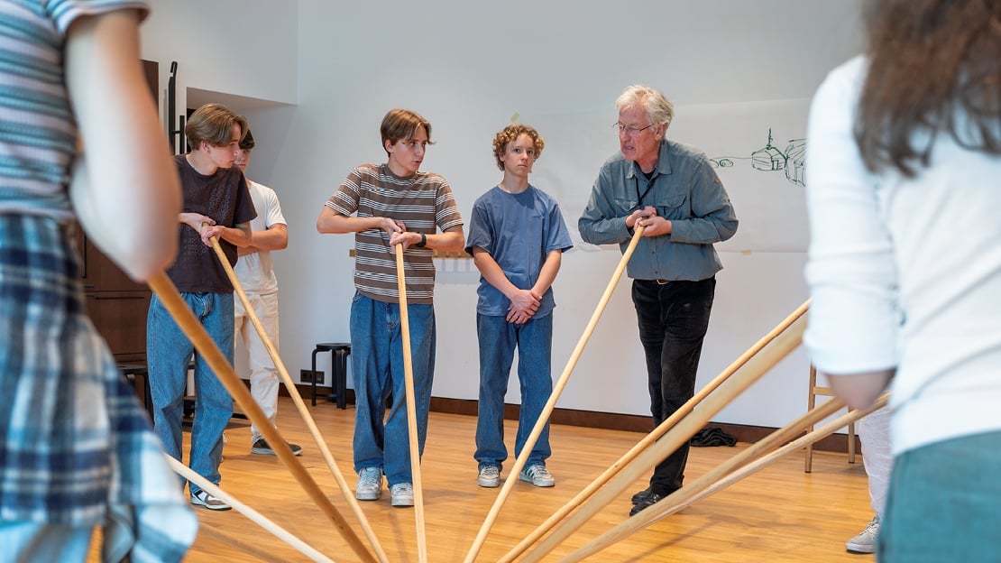 Alf Howlid står i en sirkel med elever og tester konstruksjonen til en yurt ved hjelp av stokker.