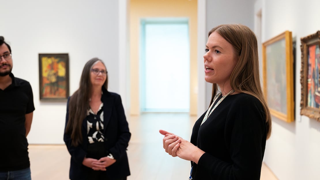 En kvinne snakker med en mann og en kvinne i et museumsrom