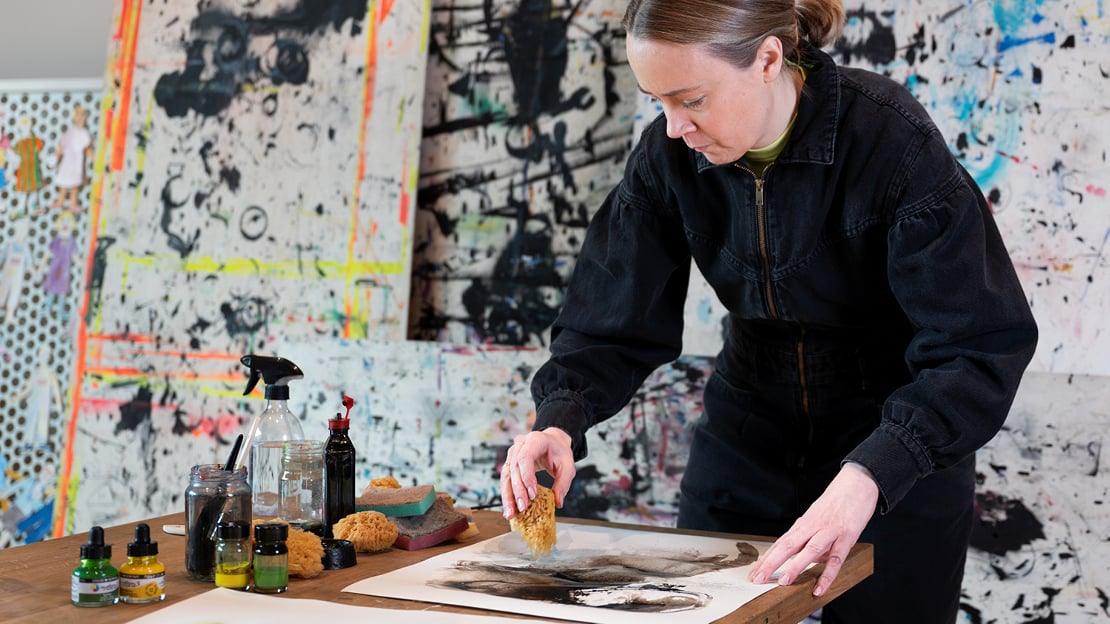 Bildet viser en kvinne i sort genser som lager kunst med blekk og svamp
