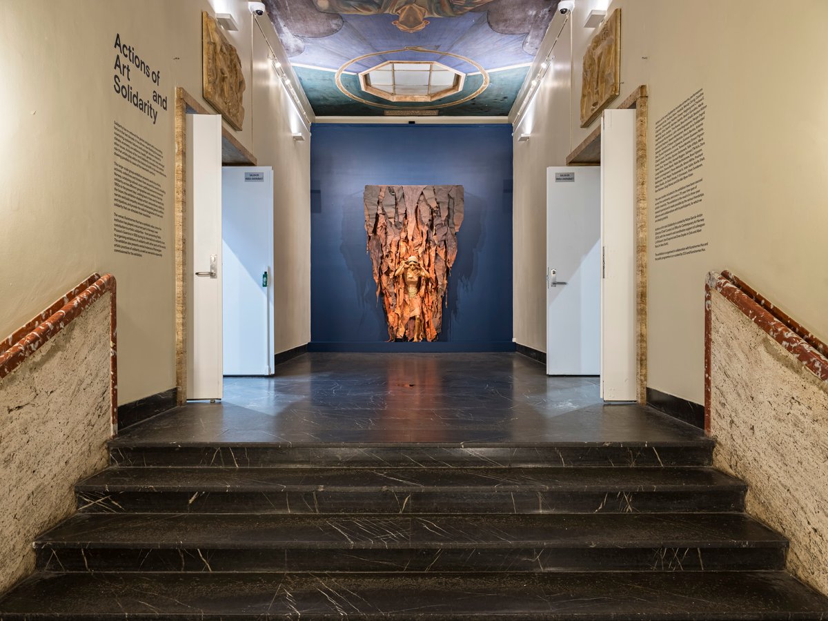 skulptur med kvinne henger på veggen ovenfor ei trapp