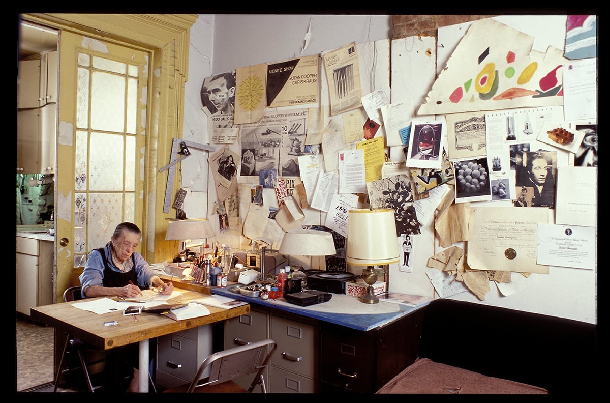 Eldre dame ved skrivebord med masse ting på veggen