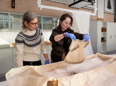 Un-boxing av Edvard Munchs babytøy. To kvinner pakker ut små klær fra esker på museum