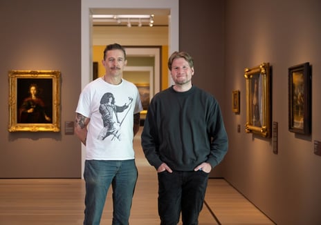 Bildet viser to menn som ser i kameraet og befinner seg i et museumsrom.
