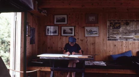 Wenche Selmer ved tegnebordet på hytta på Beltesholmen En dame sitter ved tegnebordet på en hytte