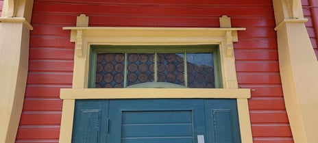 Sandsgården på Gjøvik. Detalj fra inngangsdør. Fotografi av toppen av en blå dør. Gule karmer, rød husvegg.