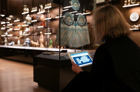 En person sitter foran et utstillingsmonter i et museum og ser på et nettbrett. 