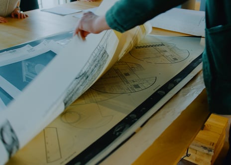 En hånd blar i arkitektplansjer.