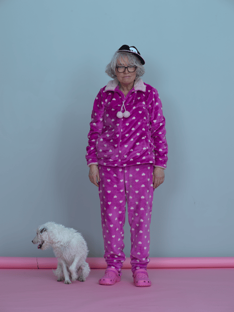 Fin Serck-Hanssen, «Lill-Ann Chepstow-Lusty», 2020 Kvinne med grått hår, caps, rosa joggedress og crocs. En hvit hund ved siden av ser vekk.