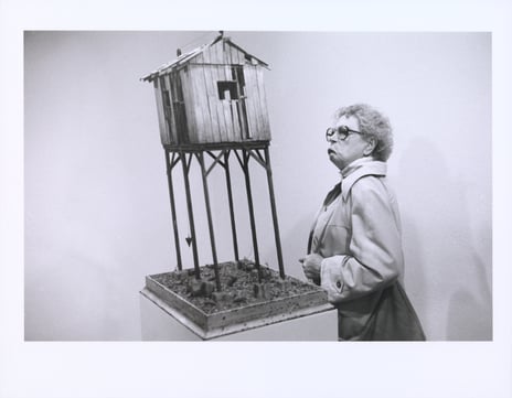 Espen Tveit «Kunst. New York 1987», 1987 svart/hvitt fotografi av mann som ser på et miniatyrhus på stolper