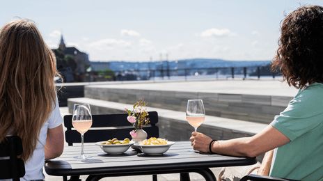 To mennesker sett bakfra sittero gs er utover Oslofjorden fra en takterrasse
