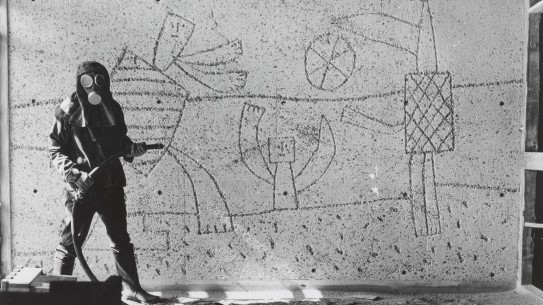 Carl Nesjar sandblåser Picassos motiver i Høyblokka, antagelig i 1959. Mann i drakt som sandblåser motiver i betongvegg