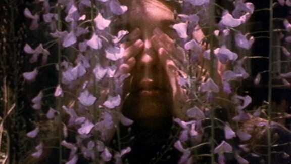 Person with hands in front of face. Purple flowers.