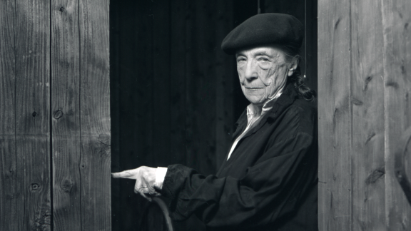 Sorthvitt portrettfoto av kunstneren Louise Bourgeois som står i en døråpning, ikledd svarte klær