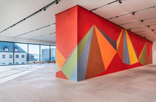 A wall painted with colourful triangles. Panoramic view of buildings and the fjord outside.