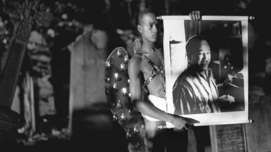 "Looking for Langston" Black and white photo of young man in cemetary, holding up a picture of Langston Hughes