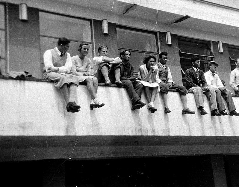 Glade, unge mennesker dingler med beina på en balkong ved Bauhaus Dessau på 1930-tallet.