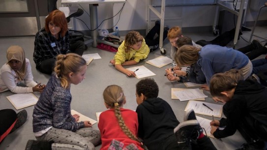Barn som ligger og sitter på gulvet og løser oppgaver på ark