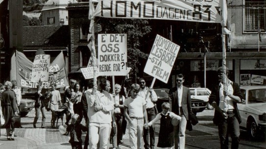 Fra homodagene i 1983. SKA/A-0009 LLH Bergen og Hordaland, Skeivt arkiv. Folk i tog med bannere som sier "Homodagene 83", "e det oss dokker e redde for!?" og "Homofile, lesbiske - stå frem"