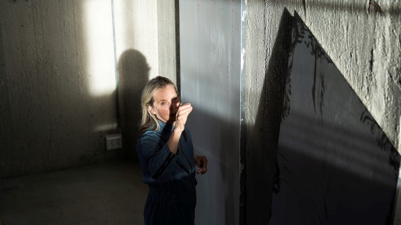 Bildet viser en kvinne som står i et rom med betongvegger. Ansiktet treffes av sollyset utenfra