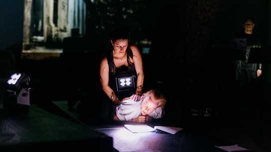 Pernille Mercury Lindstad og Rina Rosenqvist i forestillingen «Ghosting» (2024) på Trekanten. Bildet viser en scene fra et teaterstykke. En kvinne leser fra et papirark som ligger på gulvet.