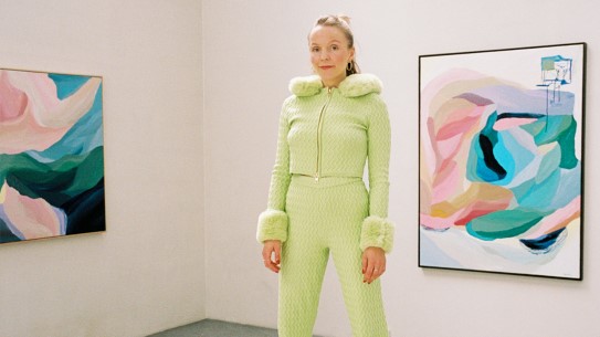 Kunstner Ragnhild Nes med fargerike malerier i bakgrunnen.