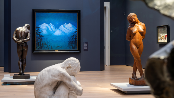 Skulpturer og malerier i et mørkeblått rom. Sentralt henger «Vinternatt i Rondane», med snødekte fjell i mange blåfarger.