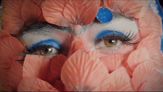 Rah Eleh, Supernova, 2018, videoinstallasjon To brune vennlige øyne ser rett inn i kameraet. de er sminket med blå øyenskygge, svart eyeliner og lange falske vipper