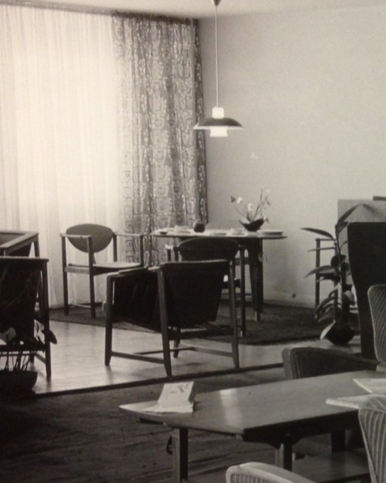 Engøs møbler for Gustav Bahus på Norway Designs For Living, Chicago 1951. En av stolene ble vist på Good Design i regi av MoMA svart-hitt bilde av interiør med stoler, bord, lampe, gardiner. blomster på bordene.