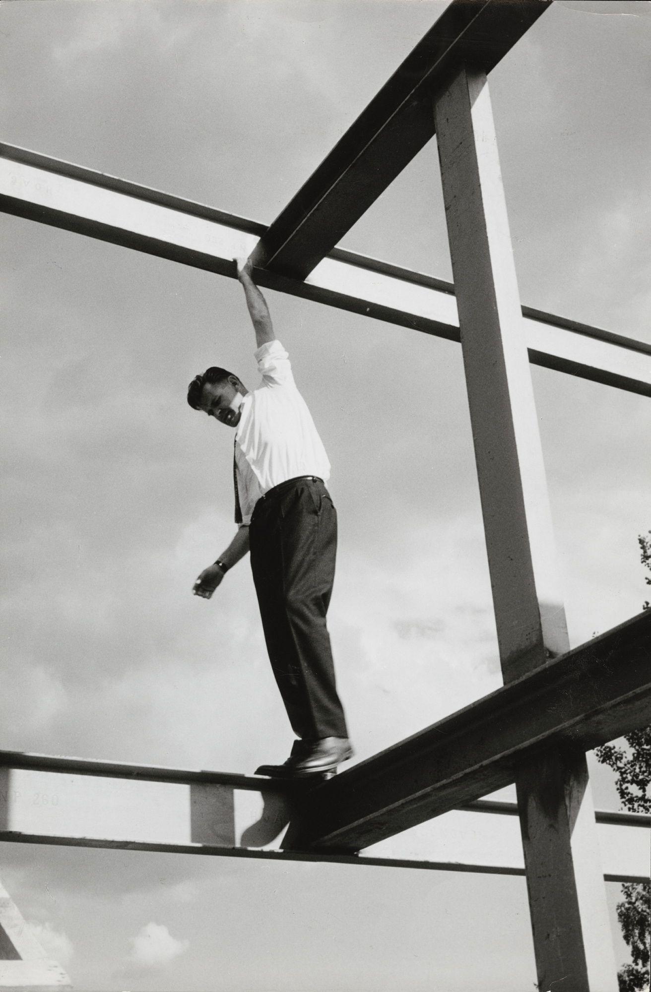 Arkitekt Geir Grung i eget hus på Jongskollen, 1963. Ukjent fotograf. Svart-hvitt foto av mann som balanserer på bjelker på et hus
