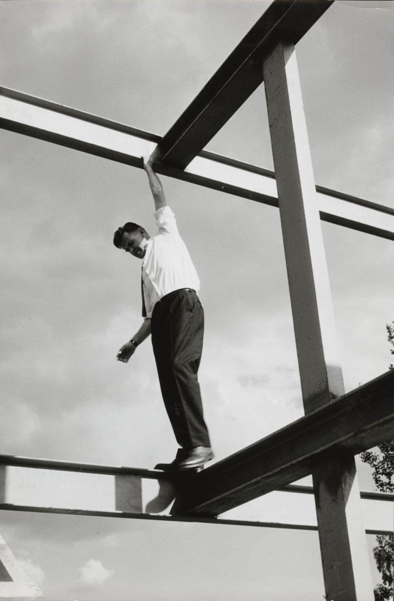 Arkitekt Geir Grung i eget hus på Jongskollen, 1963. Ukjent fotograf. Svart-hvitt foto av mann som balanserer på bjelker på et hus