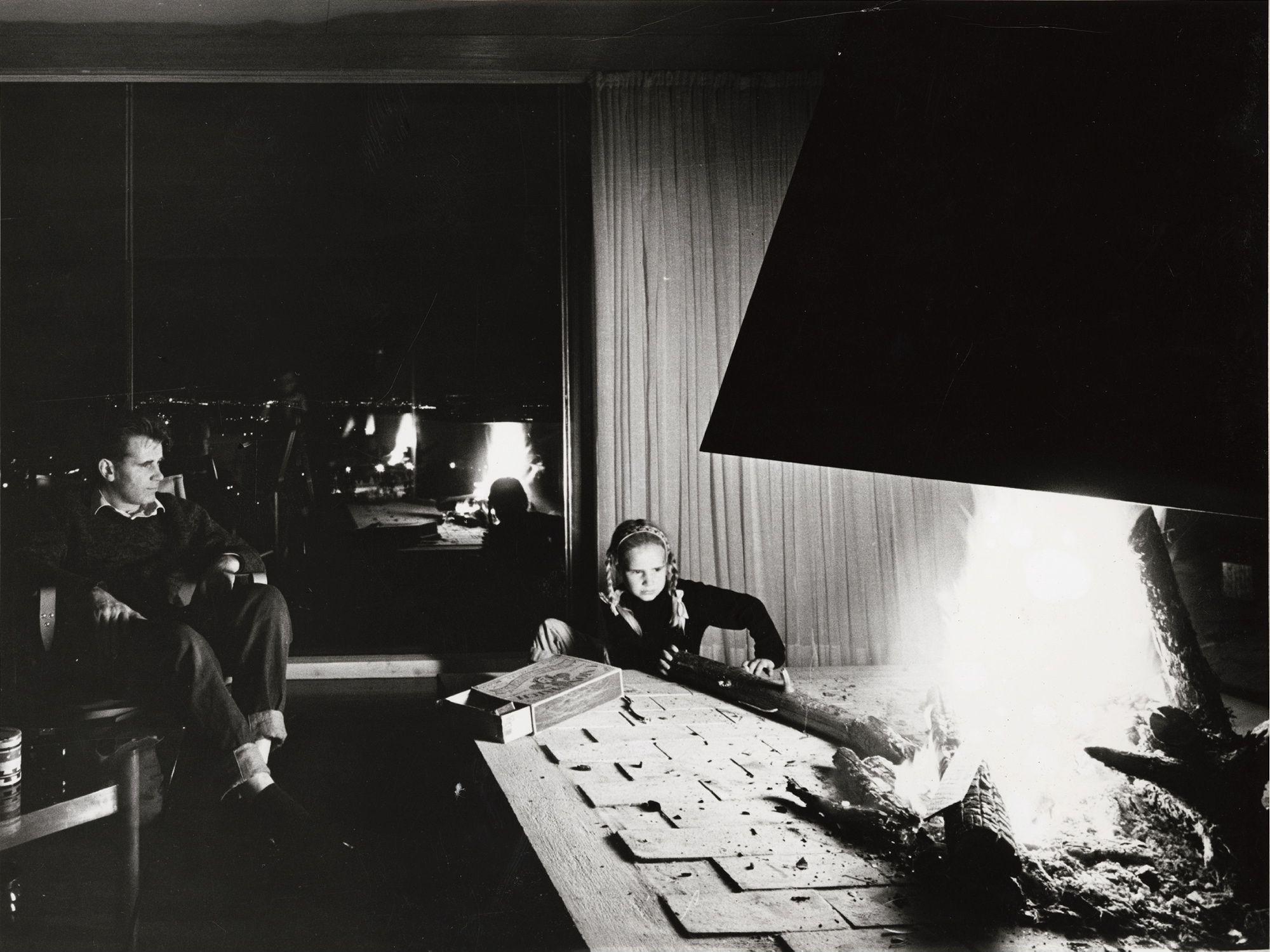 Geir Grungs eget hus på Jongskollen, 1963. Ukjent fotograf. Svart-hvitt fotografi av mann og jente foran peisen.