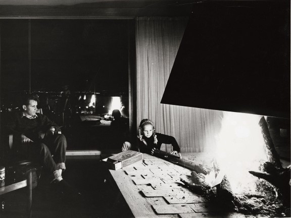 Geir Grungs eget hus på Jongskollen, 1963. Ukjent fotograf. Svart-hvitt fotografi av mann og jente foran peisen.