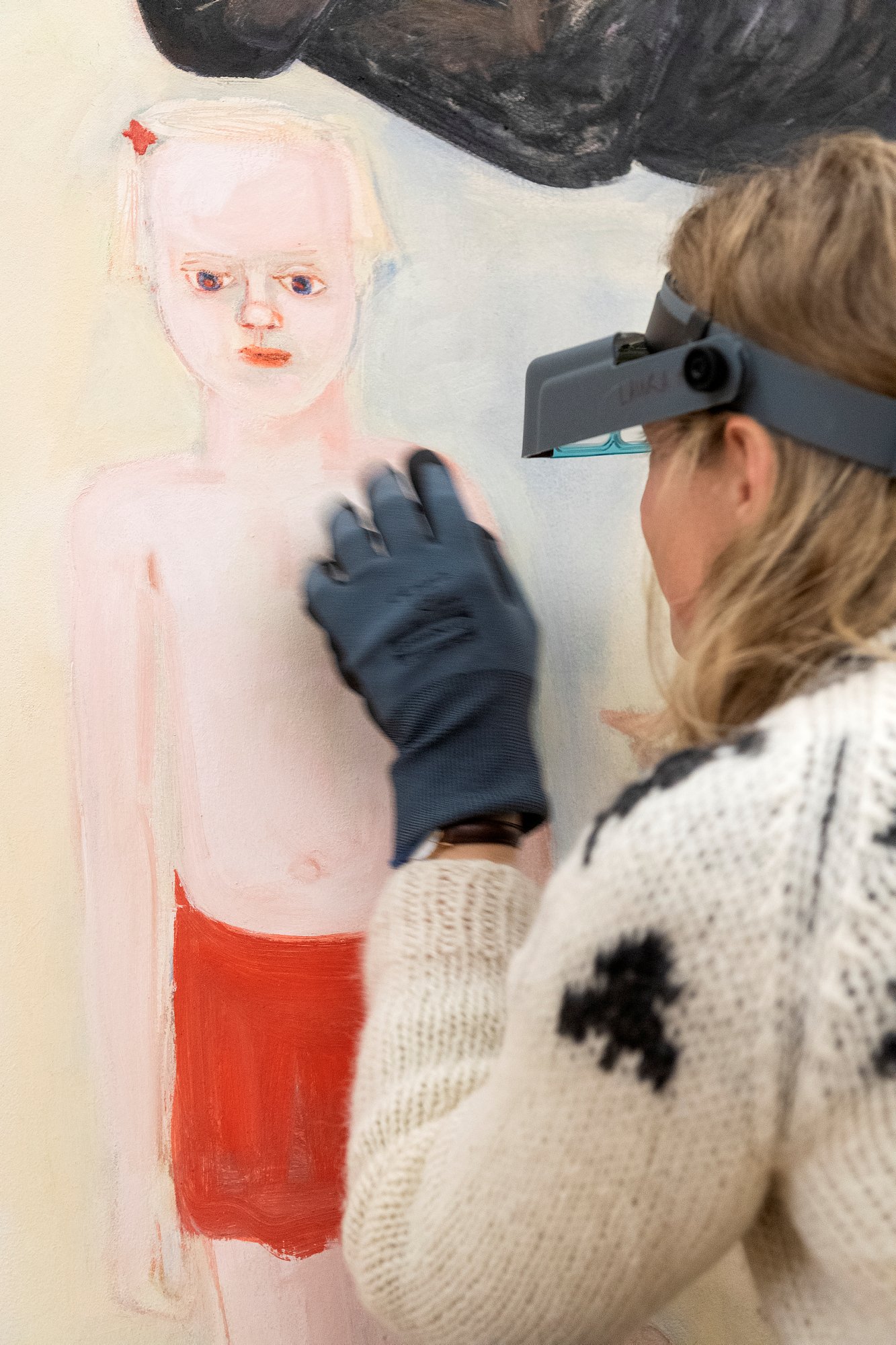 Kvinne peker på et maleri av barn i rød shorts