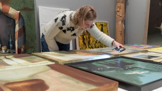 Malerikonservator Laura Homer undersøker gaven som nettopp har kommet til Nasjonalmuseet fra Galleri Dobloug. kvinne undersøker malerier med lommelykt