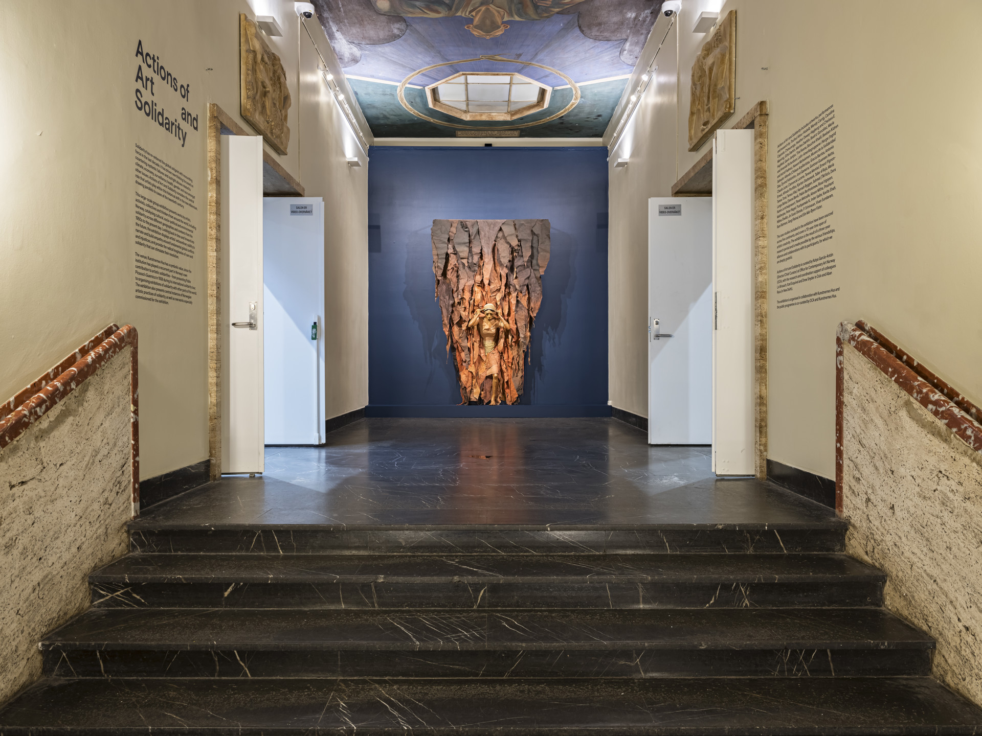 skulptur med kvinne henger på veggen ovenfor ei trapp