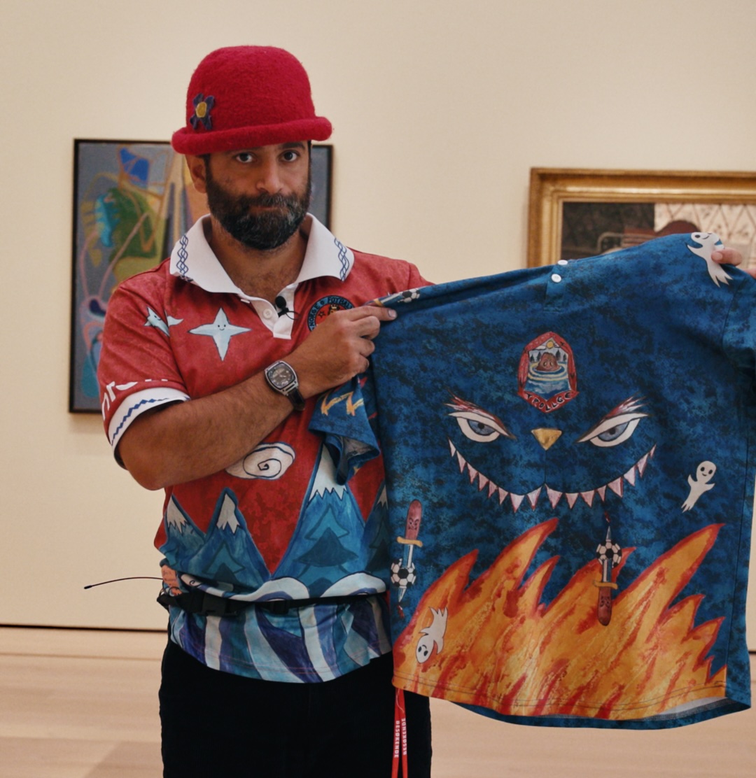 Herr Kunstmaler viser fram sin slemme landslagsdrakt i Nasjonalmuseet. Mann med rød fotballdrakt og hatt viser fram blå fotballdrakt