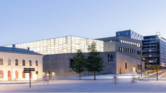 Nasjonalmuseet sett fra utsiden, med lyshallen opplyst og to trær i forkant