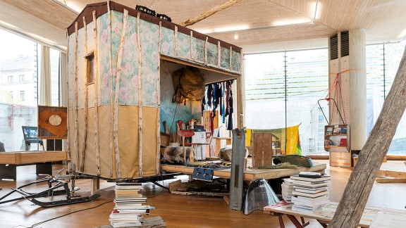 Small cabin on skis sorrounded by books, logs and different artefacts