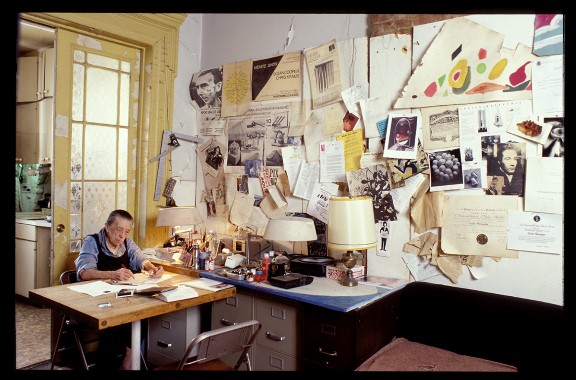Louise Bourgeois fotografert i sitt hjem i 20th Street i New York City, i 2000. Eldre dame ved skrivebord med masse ting på veggen