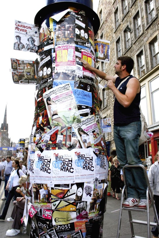 Mann henger opp plakat på en plakatsøyle i Edinburgh, 2006 – Foto: Jeff J. Mitchell / Getty Images